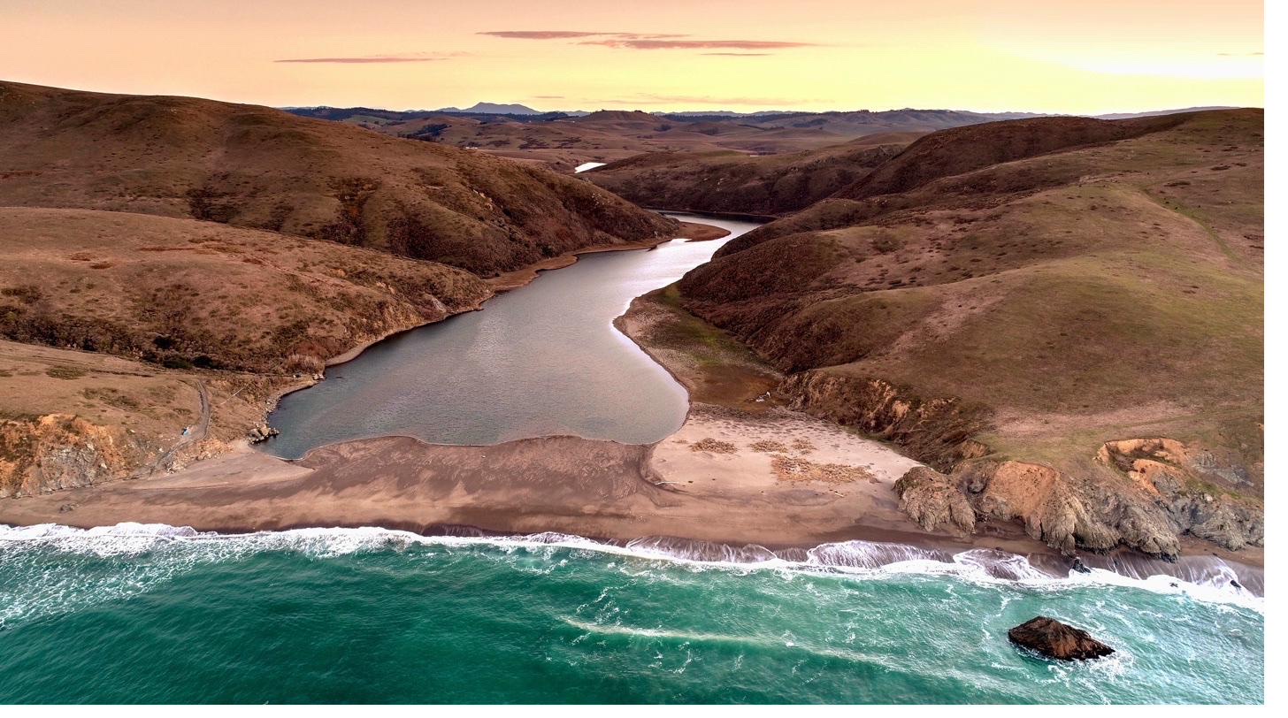 Aerial view of the Estero Americano meeting the Pacific Ocean at sunset